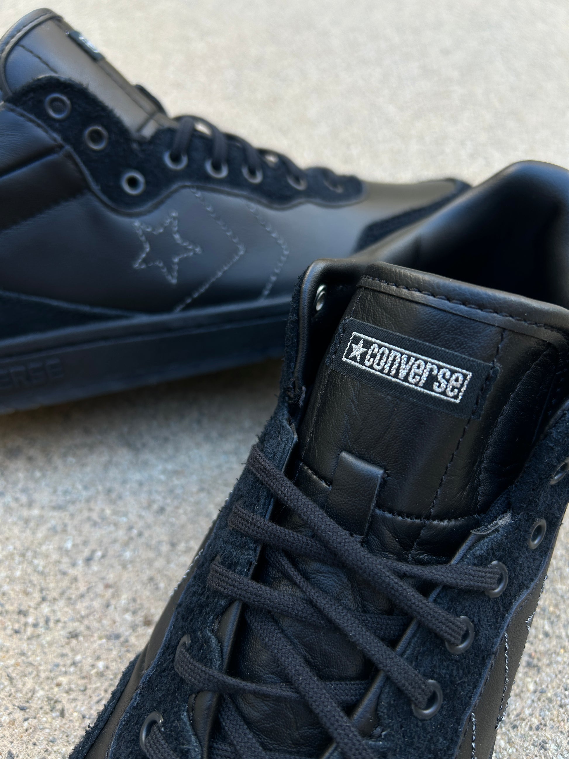 Black Converse shoes with laces on a light gray surface