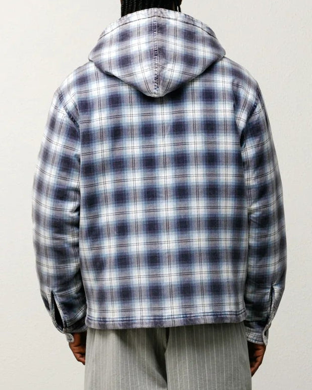 Person wearing a plaid jacket and gray shorts standing against a white wall.