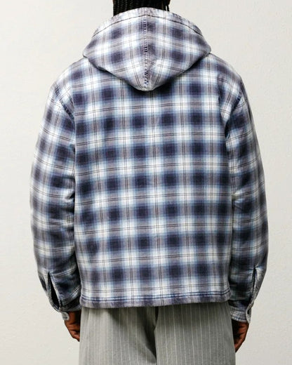 Person wearing a plaid jacket and gray shorts standing against a white wall.