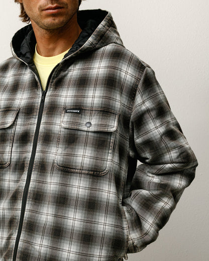 Person wearing a gray and black plaid jacket with a visible brand logo on a plain background