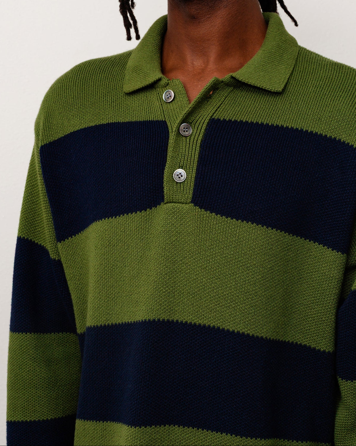 A close-up of a person wearing a ribbed knit polo sweater with horizontal olive green and navy blue stripes, featuring a three-button placket.