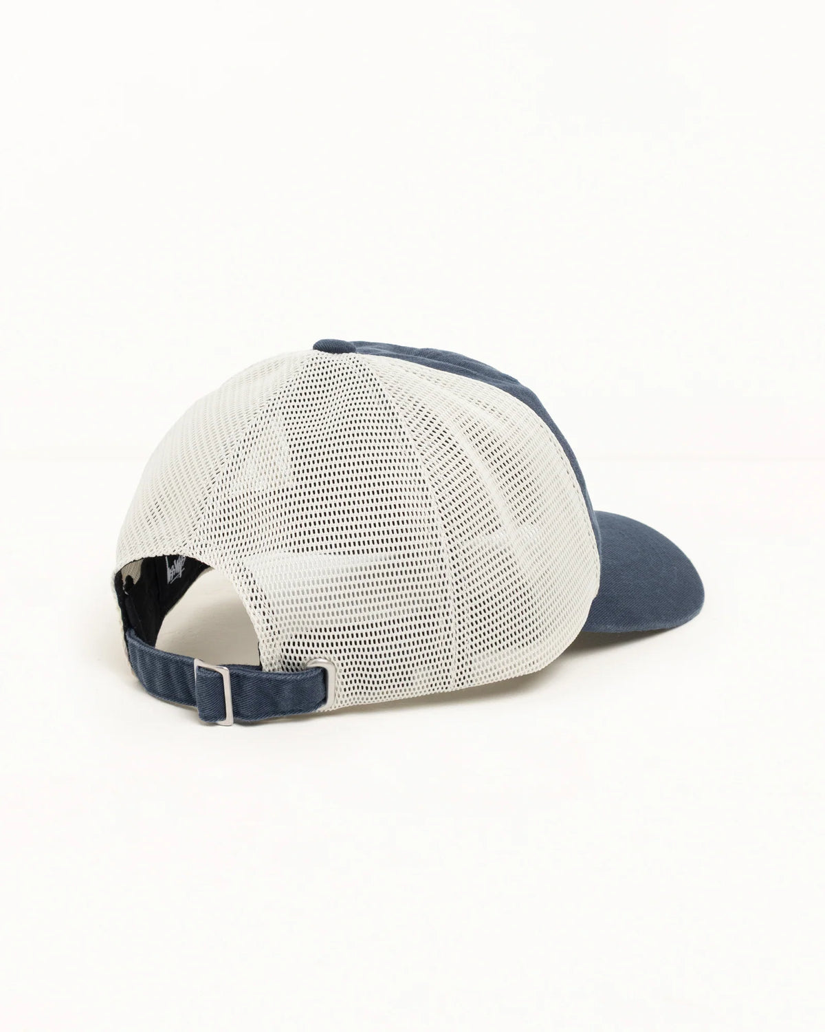 A rear three-quarter view of a trucker-style baseball cap with a white mesh back and navy blue front panel, visor, and adjustable strap, set against a plain white background.