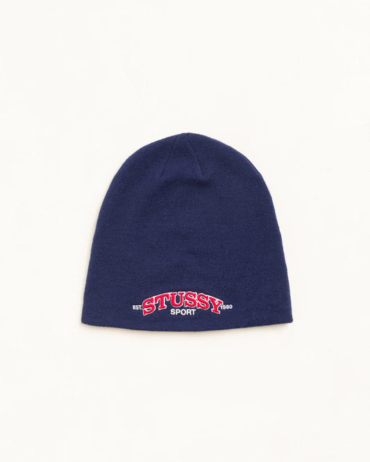 A navy blue knit beanie hat featuring an embroidered 'STUSSY SPORT' logo in red and white on the front cuff, set against a plain off-white background.
