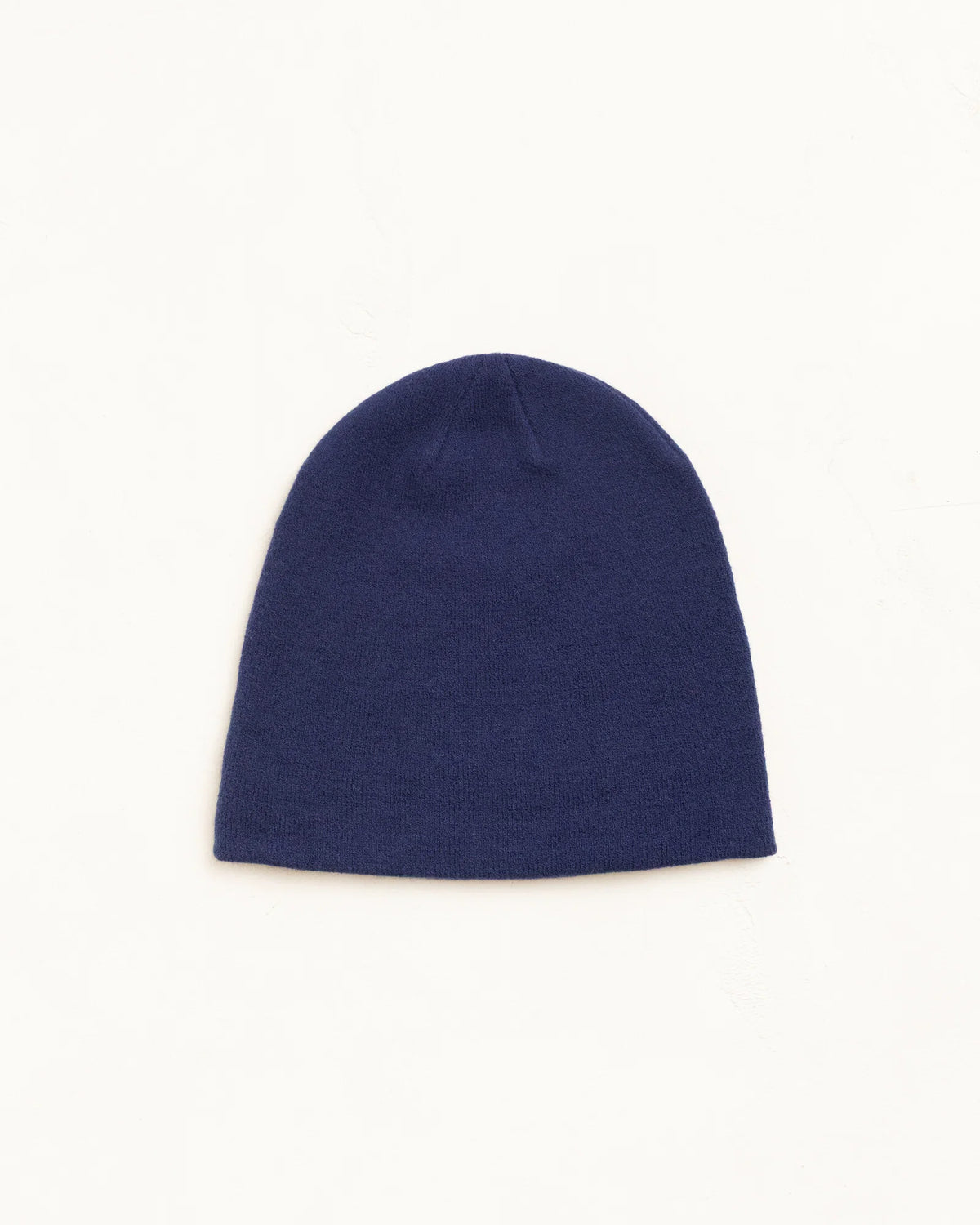 A solid navy blue knit beanie hat, photographed flat against a clean, off-white background.
