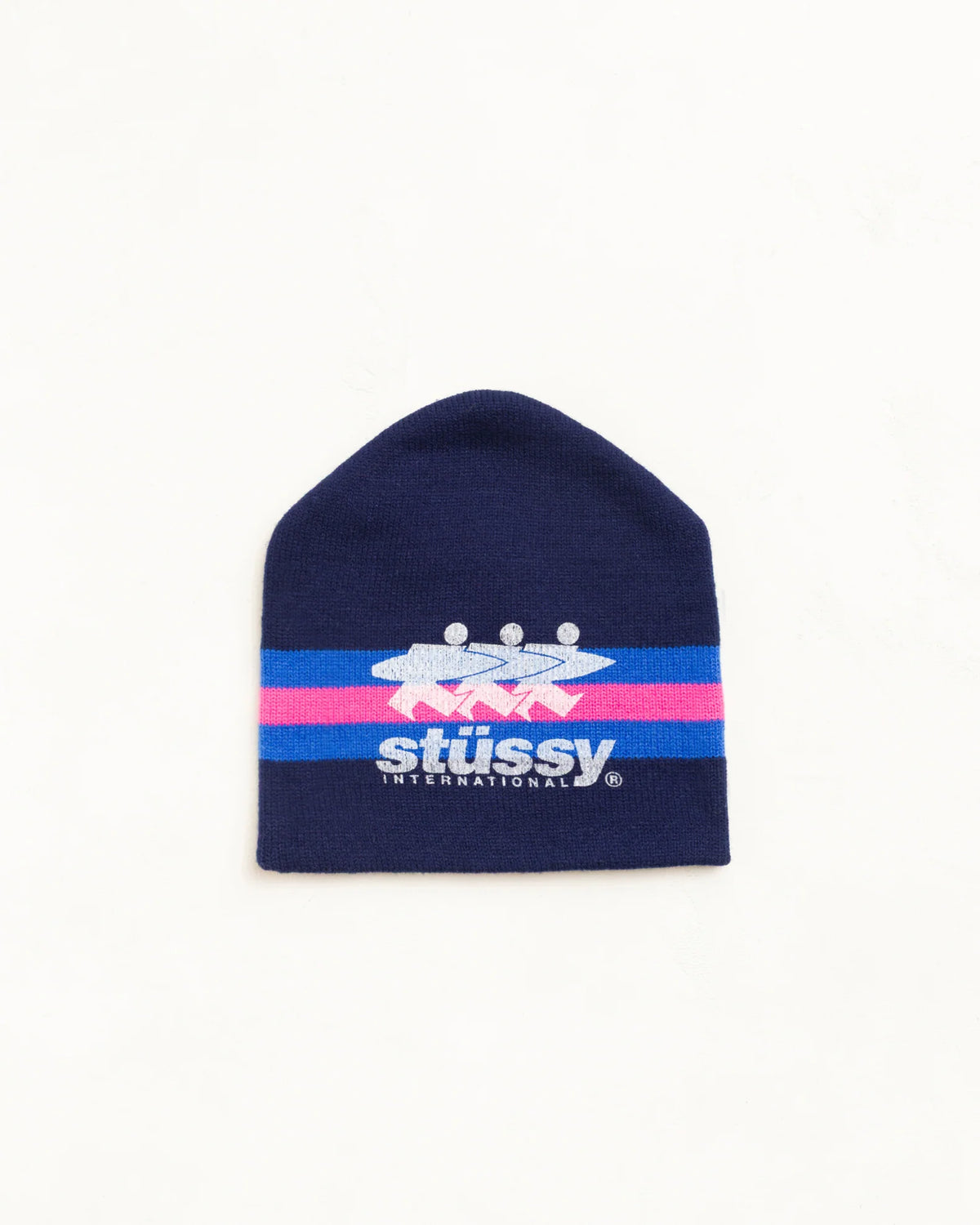 A navy blue knit beanie hat featuring a horizontal stripe design with pink and light blue bands, and the Stussy logo printed in white and blue across the center.