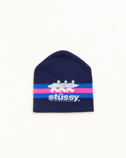 A navy blue knit beanie hat featuring a horizontal stripe design with pink and light blue bands, and the Stussy logo printed in white and blue across the center.