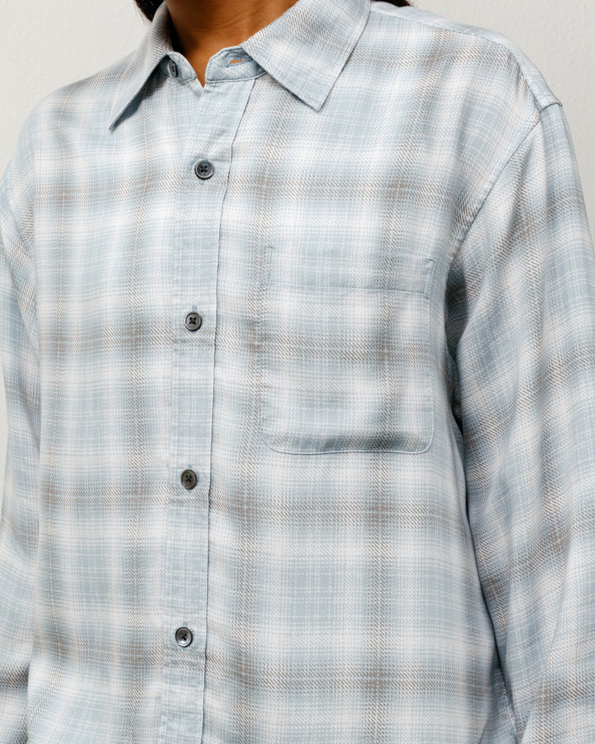 Person wearing a light blue plaid shirt against a neutral background