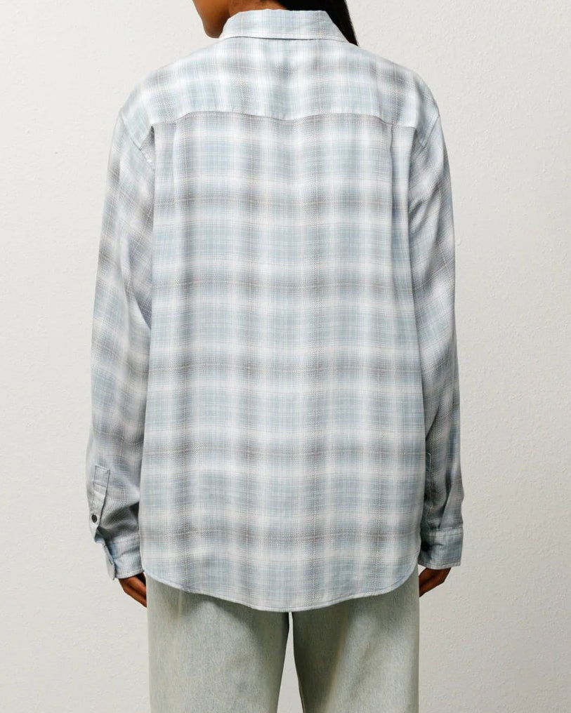 Person wearing a checkered shirt and light-colored pants against a plain background