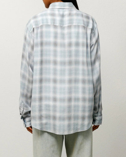 Person wearing a checkered shirt and light-colored pants against a plain background
