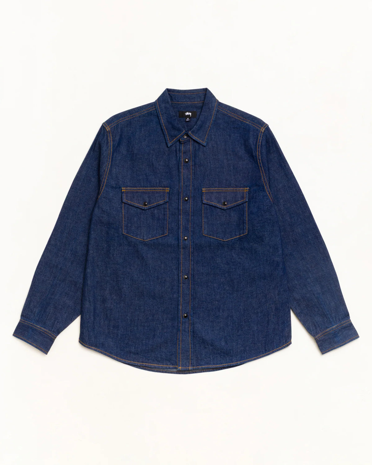 A dark indigo denim long-sleeve button-up shirt with two buttoned chest pockets, laid flat against a clean white background.