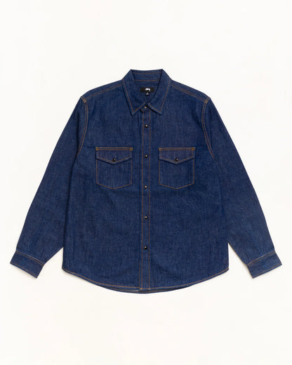 A dark indigo denim long-sleeve button-up shirt with two buttoned chest pockets, laid flat against a clean white background.