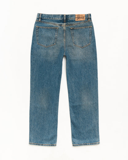 Back view of a pair of blue denim jeans with a straight-leg fit, showing the back pockets and a brown leather brand patch on the waistband.