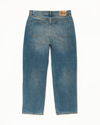 Back view of a pair of blue denim jeans with a straight-leg fit, featuring classic five-pocket styling and a visible Stüssy brand patch on the back waistband.