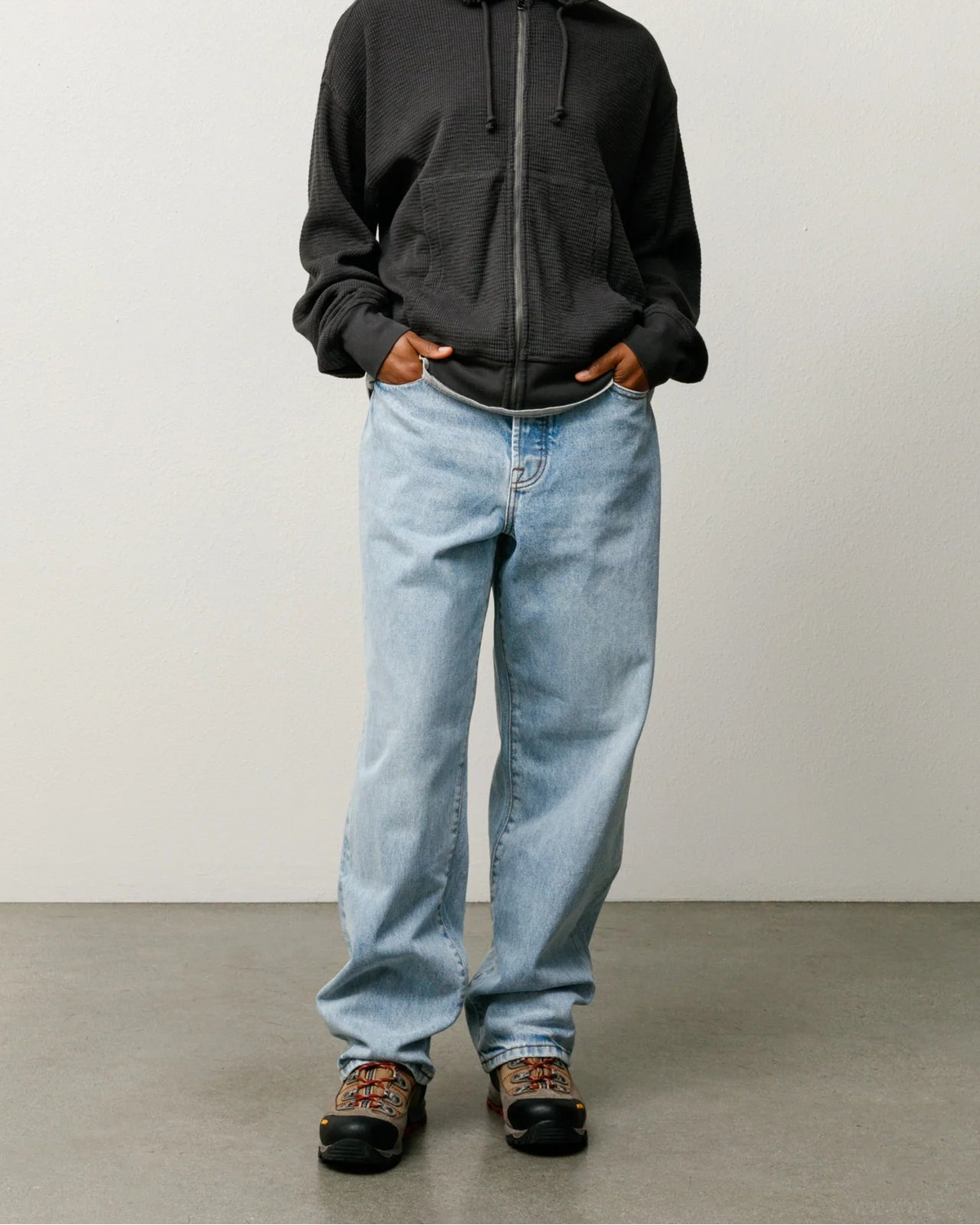 A model wearing a black zip-up hoodie, light-wash wide-leg jeans, and black shoes, standing against a neutral studio background.