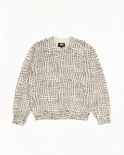 A cream-colored knit sweater with a black grid pattern, laid flat against a solid white background.