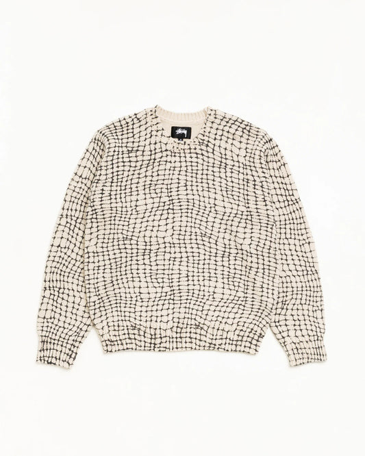 A cream-colored knit sweater with a black grid pattern, laid flat against a solid white background.